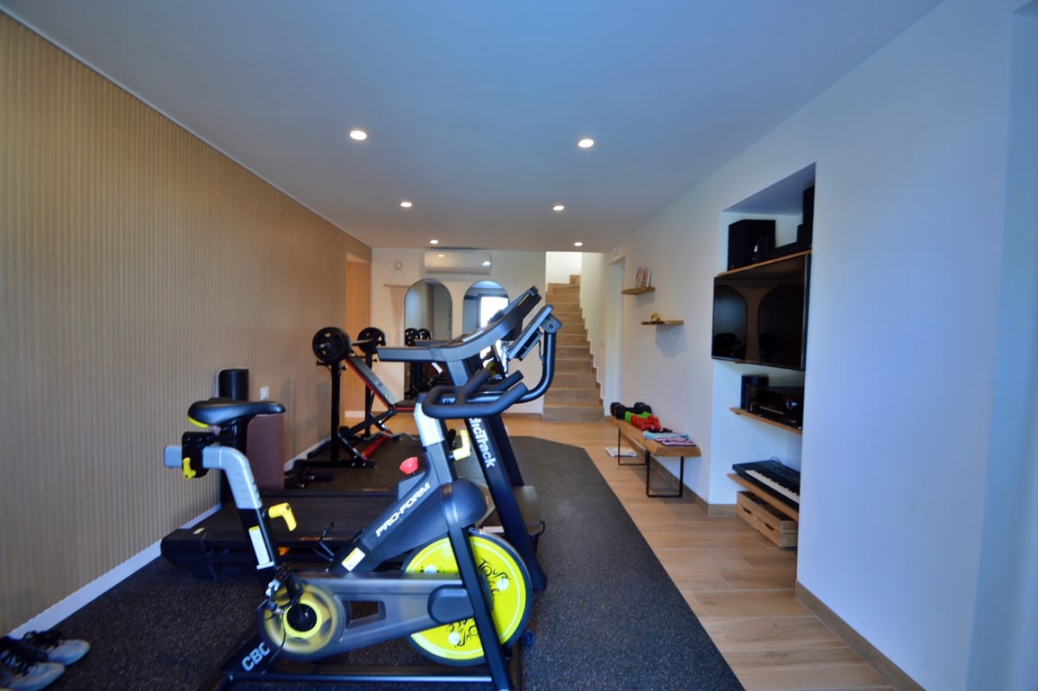 Salle de sport privée équipée d'un vélo de spinning et d'un tapis de course, avec mur en bois latté, éclairage encastré et espace multimédia dédié.