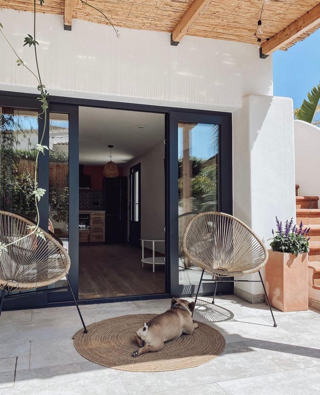 Terrasse ombragée avec plafond en canisse et poutres en bois, offrant un accès direct à l'espace de vie par de larges baies vitrées coulissantes.