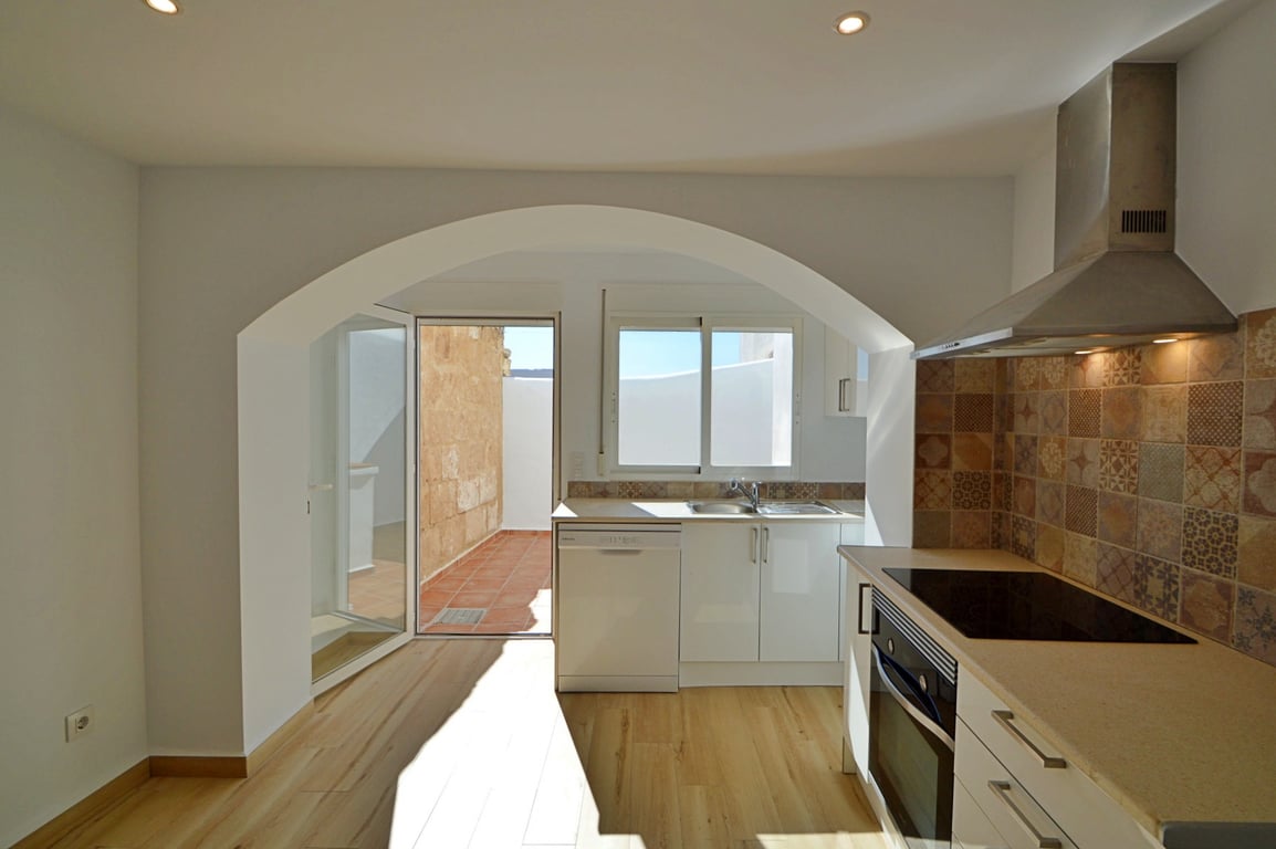 Cuisine moderne avec arche décorative, crédence en carreaux de ciment et accès direct à un patio privé en terre cuite baigné de lumière naturelle.