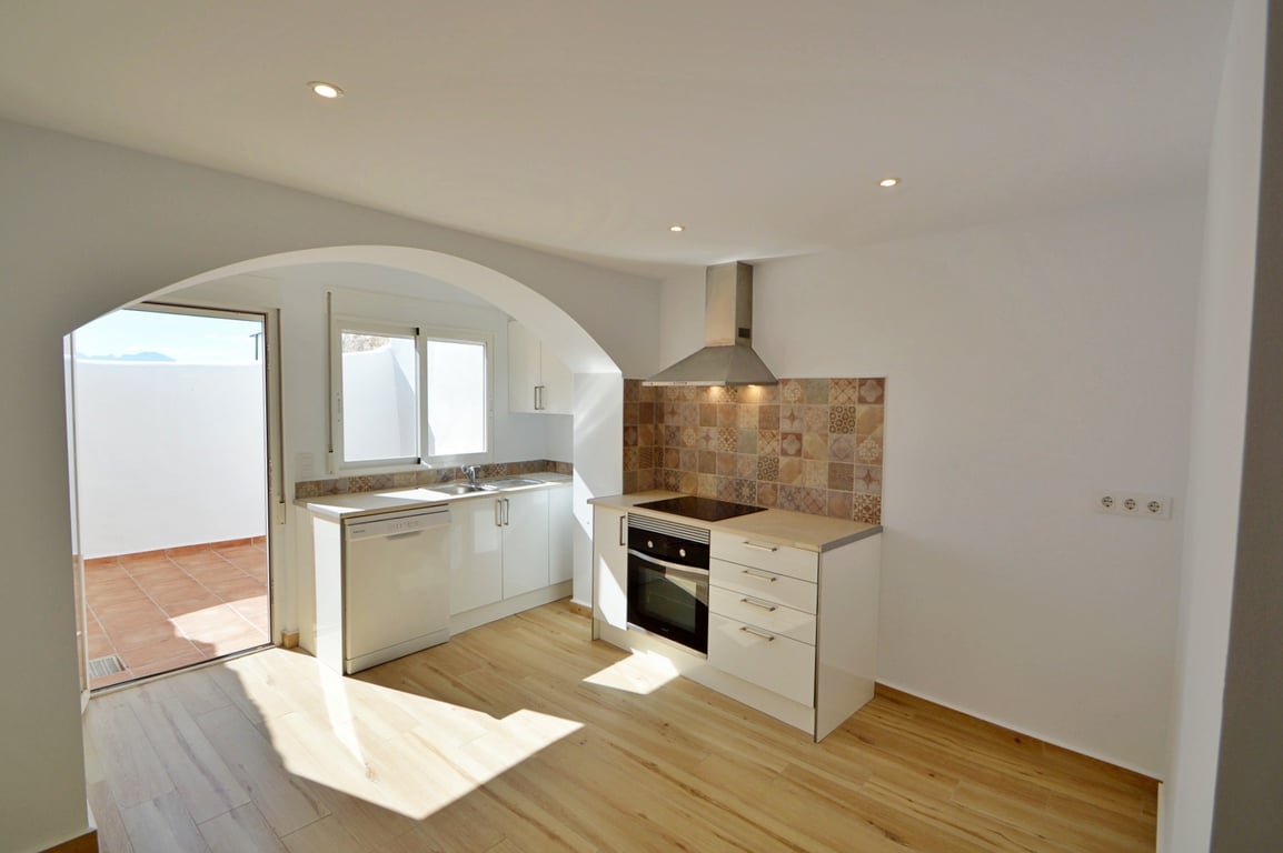 Cuisine moderne rénovée avec meubles blancs, crédence en carreaux de ciment et accès direct à un patio privé ensoleillé.