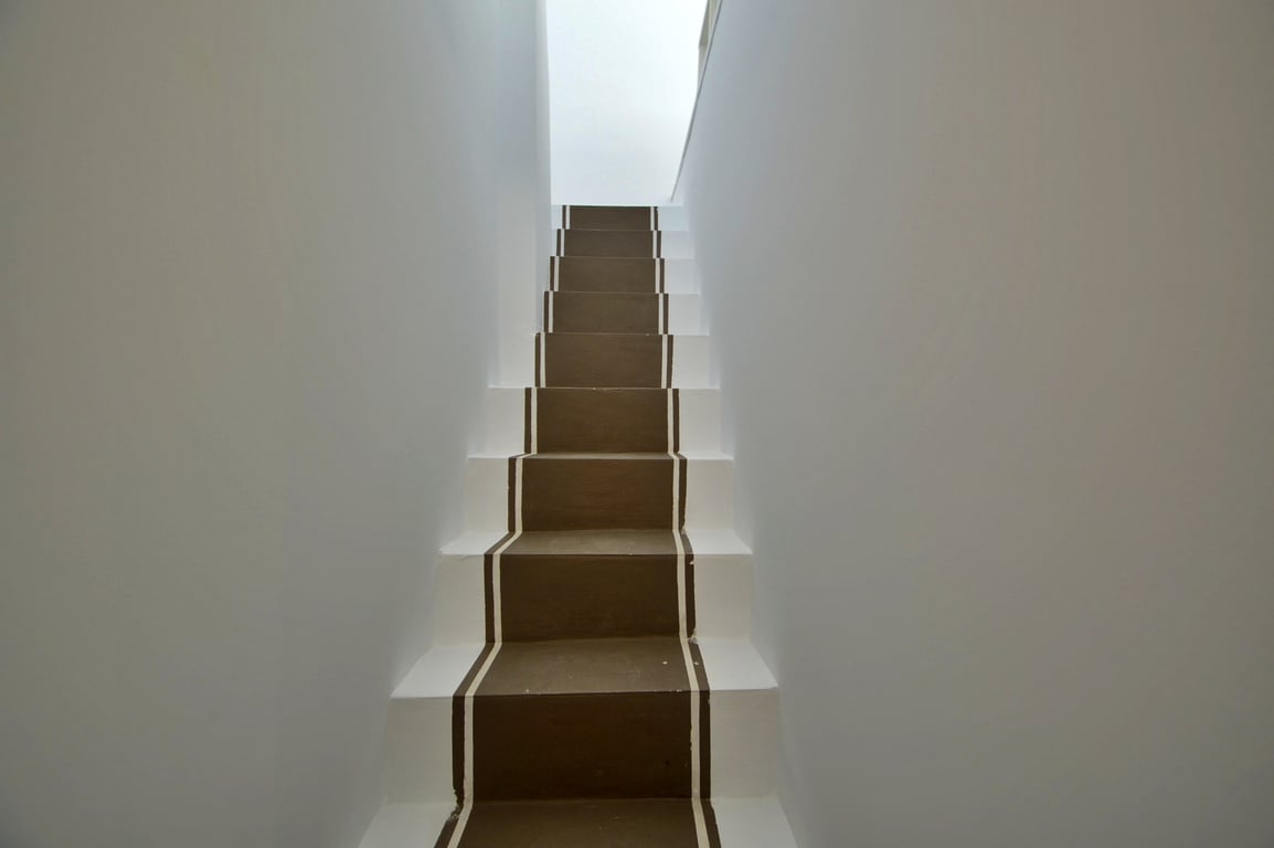 Escalier intérieur au design minimaliste avec des marches peintes en marron et bordures blanches, éclairé par une lumière naturelle.