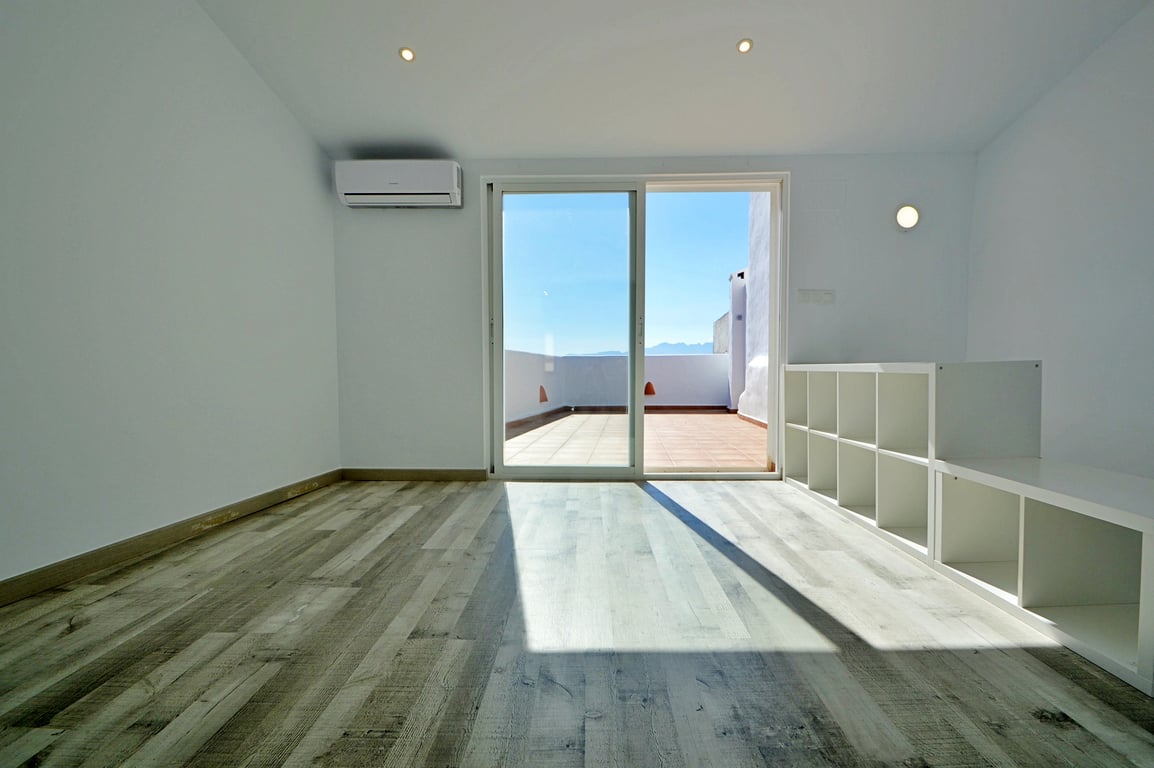 Espace lumineux avec sol en stratifié, climatisation et accès direct à la terrasse de toit par une baie vitrée coulissante.