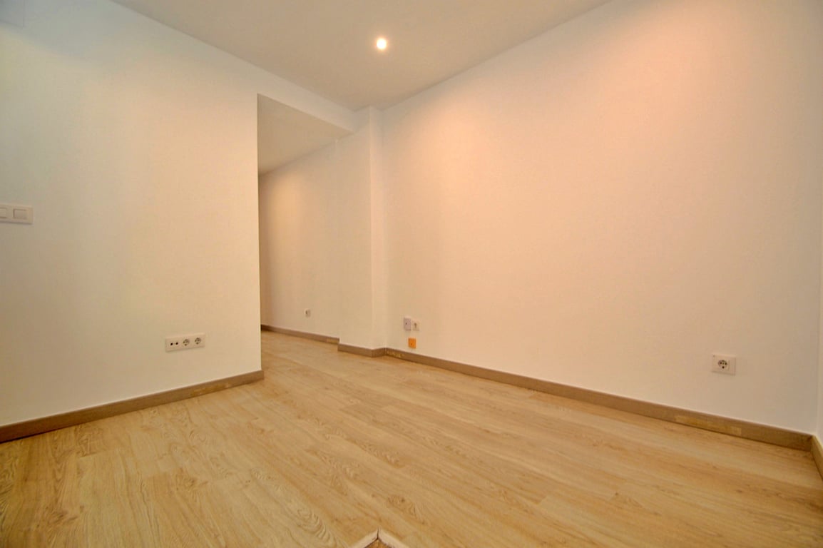 Espace polyvalent rénové avec sol en stratifié clair, murs blancs lisses et éclairage par spots encastrés au plafond.