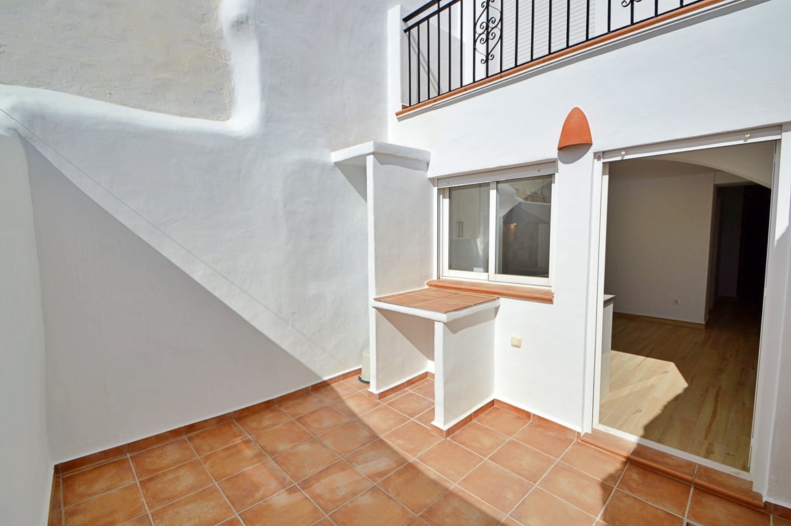 Patio privé avec sol en terre cuite, murs blanchis à la chaux et un plan de travail extérieur intégré. Une porte vitrée offre un accès direct à l'intérieur.