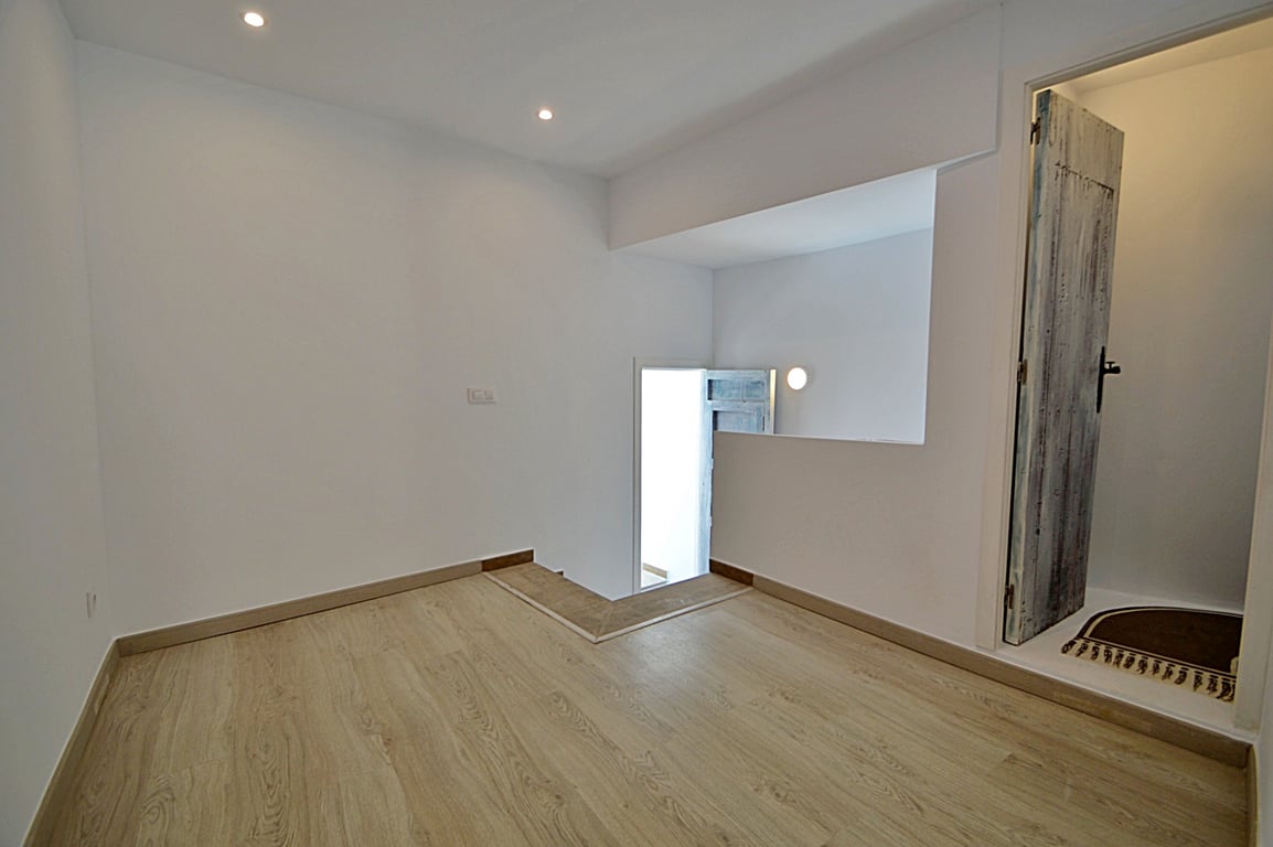 Pièce intermédiaire polyvalente avec parquet clair, spots encastrés au plafond et une porte en bois d'aspect rustique restauré.