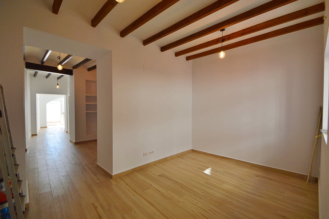Pièce lumineuse avec poutres en bois apparentes, parquet clair et murs blancs. L'éclairage suspendu et la disposition ouverte créent une atmosphère spacieuse et moderne.