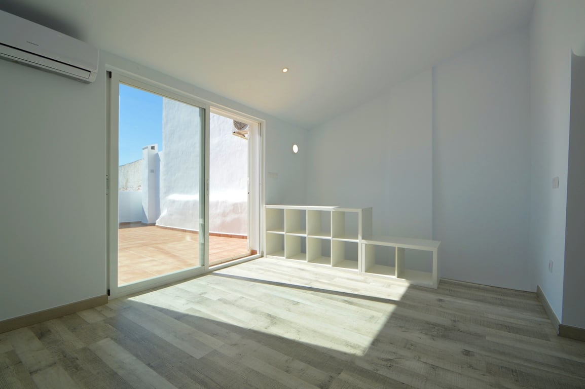 Pièce lumineuse avec sol en bois clair, climatisation et accès direct à une terrasse carrelée par de grandes baies vitrées coulissantes.