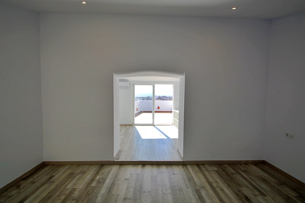 Pièce polyvalente avec parquet au sol, spots encastrés et une ouverture voûtée menant à un espace lumineux avec accès à la terrasse.