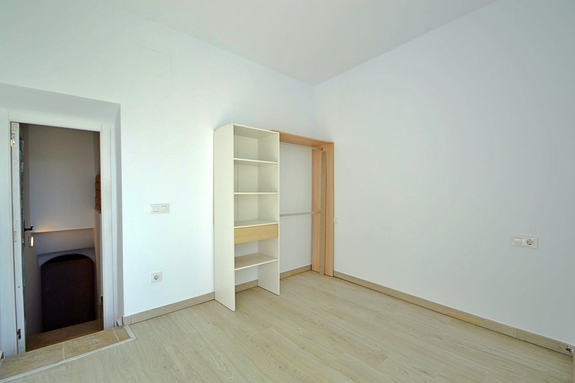 Pièce polyvalente avec sol en grès imitation bois, murs blancs et étagère ouverte avec penderie, située à côté de l'accès aux escaliers.