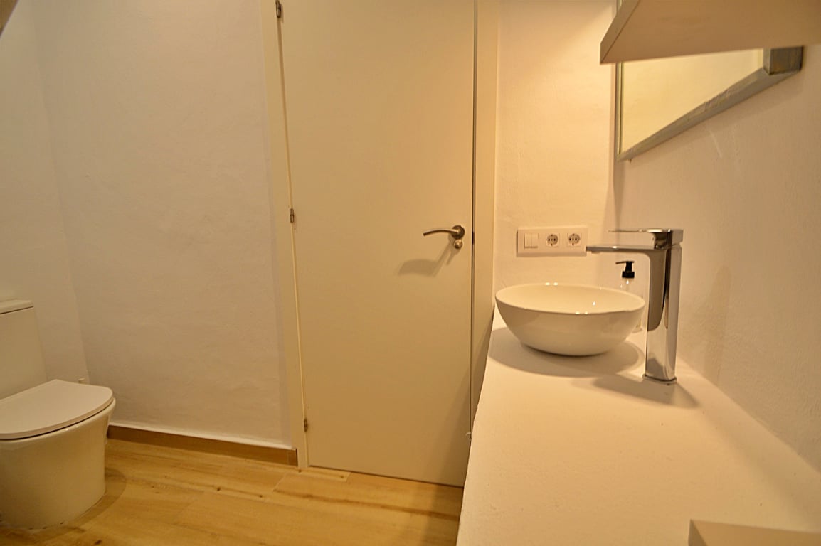 Salle d'eau moderne avec vasque à poser circulaire, robinetterie chromée et sol en bois clair. Le design minimaliste offre des murs blancs et des sanitaires contemporains.