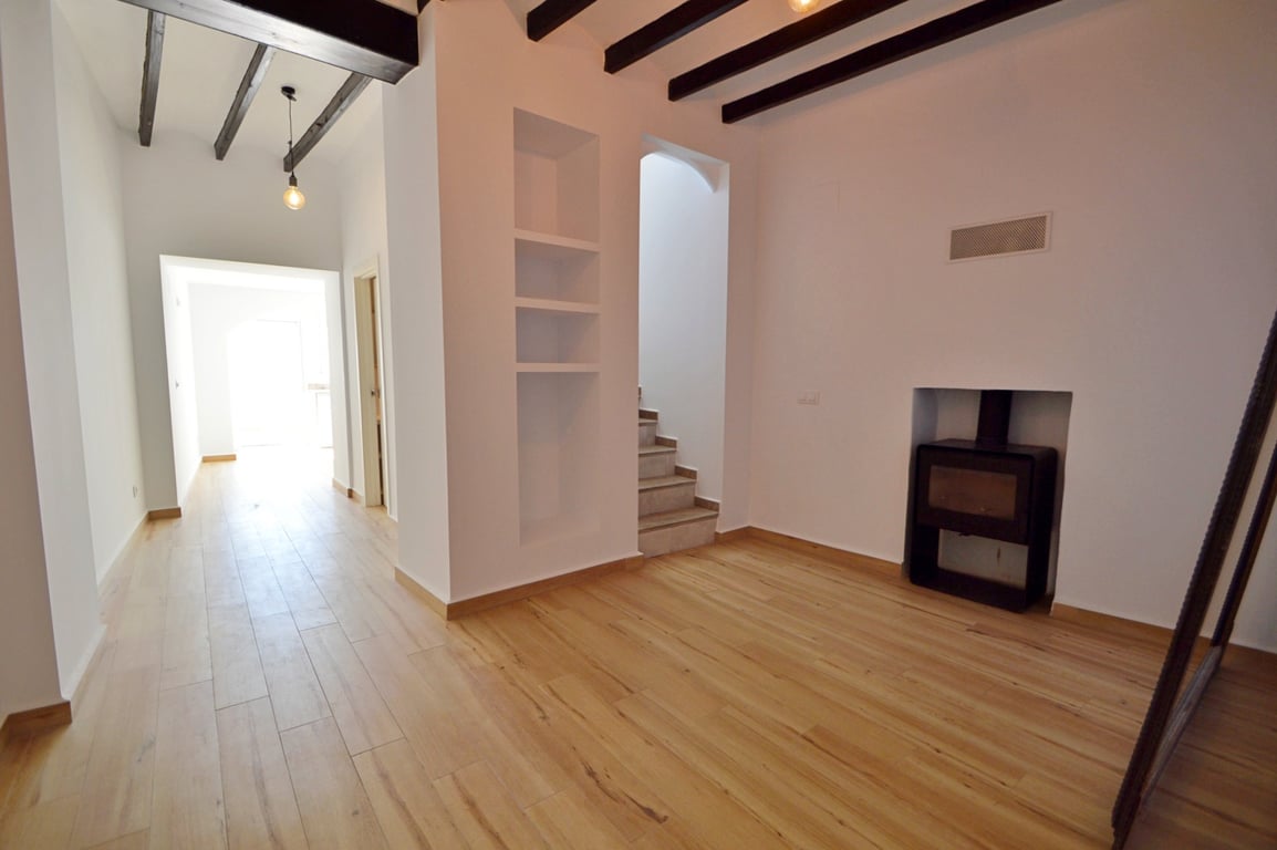 Salon avec poutres apparentes sombres, parquet clair et poêle à bois encastré. Dispose d'étagères murales intégrées et d'un escalier menant à l'étage.
