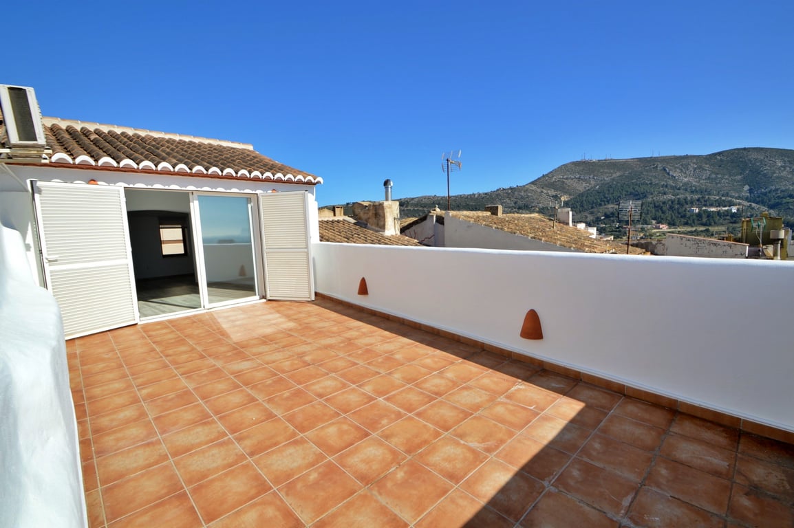 Vaste terrasse sur le toit avec carrelage en terre cuite, murs blancs et vue panoramique sur les montagnes environnantes.