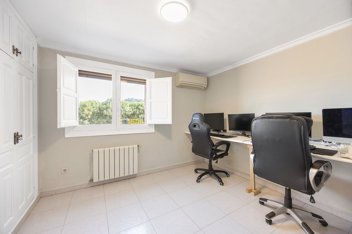 Bureau lumineux avec placards intégrés, climatisation et radiateur. La fenêtre avec volets intérieurs offre une vue sur le jardin et une belle luminosité naturelle.