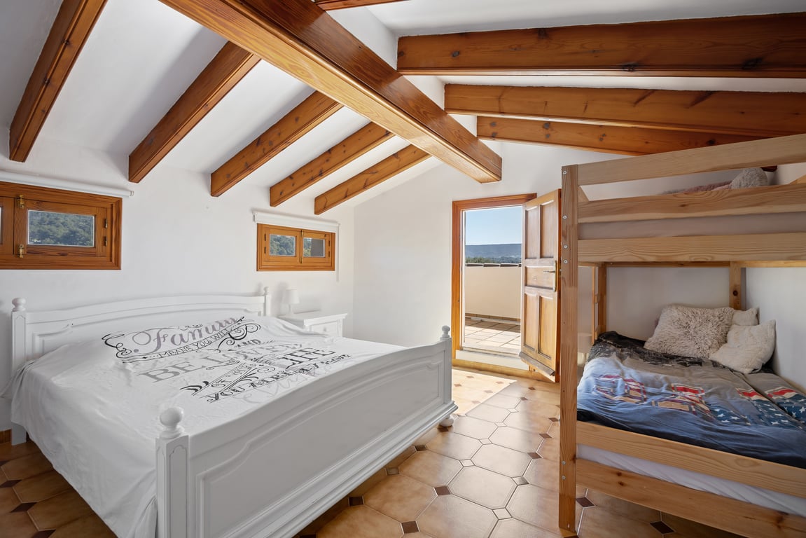 Chambre en mezzanine avec poutres en bois apparentes, sol en terre cuite et accès à une terrasse privée. Elle dispose d'un lit double et de lits superposés en bois.