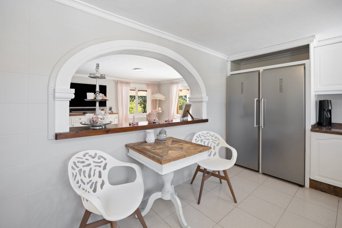 Cuisine avec arche ouverte sur le séjour, équipée d'un double réfrigérateur en inox et d'un coin repas avec table en bois et chaises modernes.