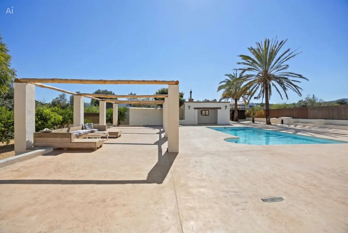Espace piscine avec vaste terrasse dallée, pergola aux poutres en bois rustique et coin salon extérieur entouré de palmiers et de végétation méditerranéenne.