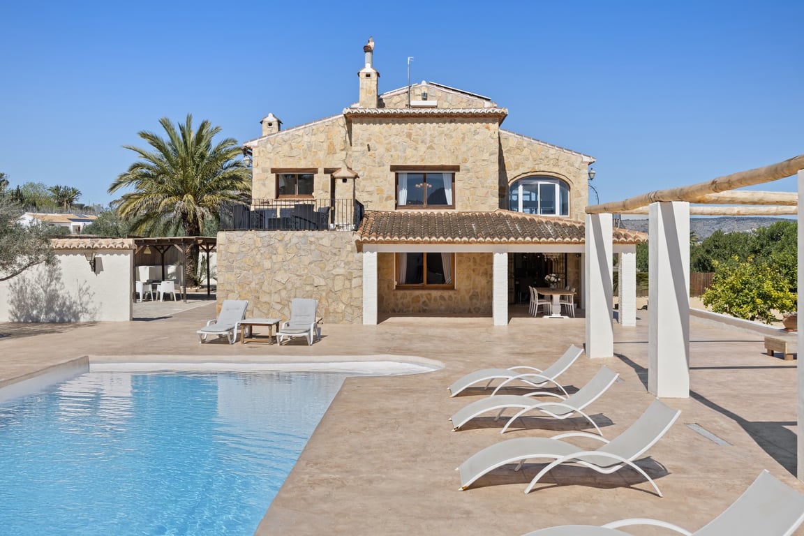 Façade en pierre naturelle avec naya couverte, vaste terrasse carrelée et piscine. La villa dévoile son architecture sur deux niveaux et ses espaces de détente extérieurs.