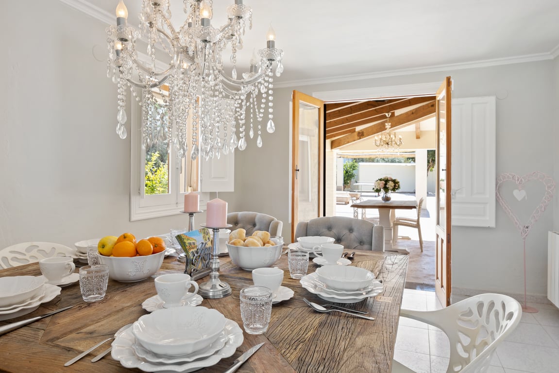 Salle à manger lumineuse avec table en bois rustique et lustre en cristal, offrant un accès direct à la naya couverte par des portes-fenêtres.