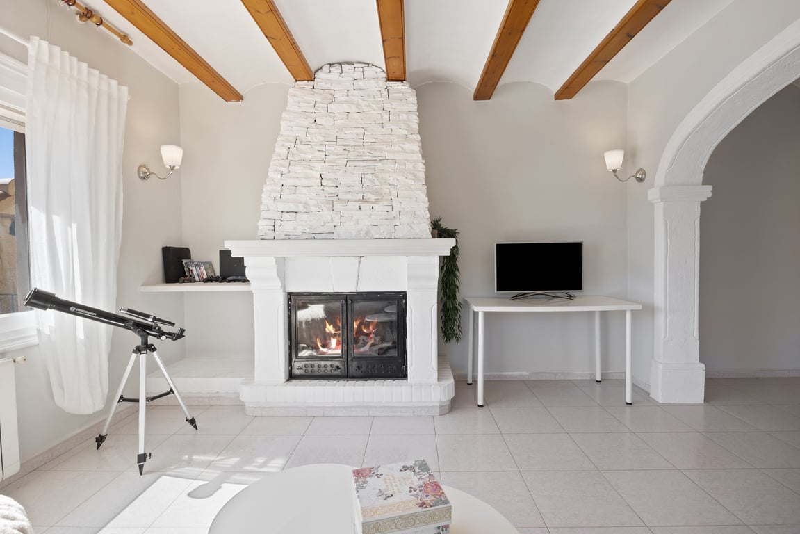 Salon avec cheminée en pierre blanche, poutres en bois apparentes au plafond et une arche en pierre traditionnelle reliant les espaces.