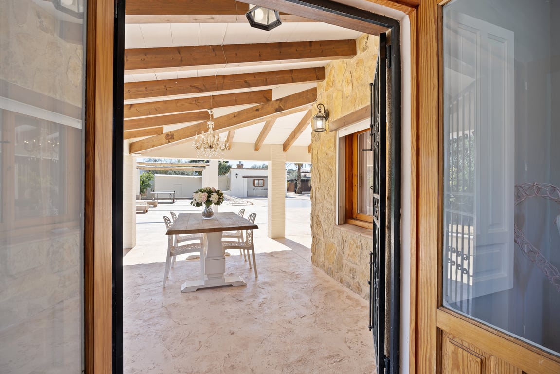 Terrasse couverte avec poutres en bois apparentes, murs en pierre naturelle et espace dînatoire extérieur face à la piscine.