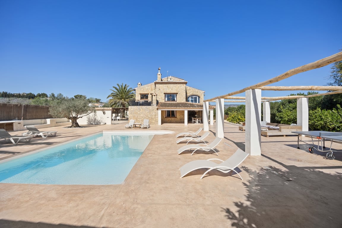 Vue extérieure de la villa en pierre avec piscine de 5x10m, vaste terrasse ensoleillée, pergola et espace de loisirs avec table de ping-pong.