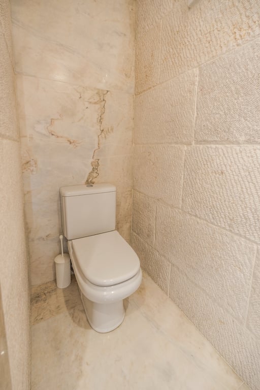 Cabinet de toilette avec murs en pierre calcaire texturée et marbre poli, alliant matériaux naturels et design épuré.