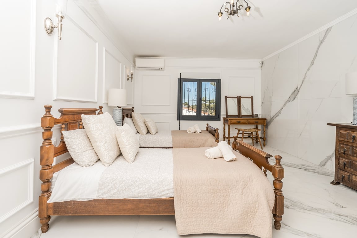 Chambre avec deux lits en bois sculpté, sol en marbre veiné et moulures murales classiques. Elle dispose d'une coiffeuse en bois et de la climatisation.