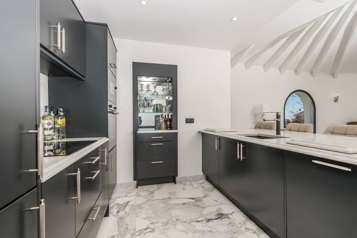 Cuisine contemporaine aux finitions sombres avec plans de travail en marbre et îlot central. Comprend un bar intégré et un plafond aux poutres apparentes décoratives.