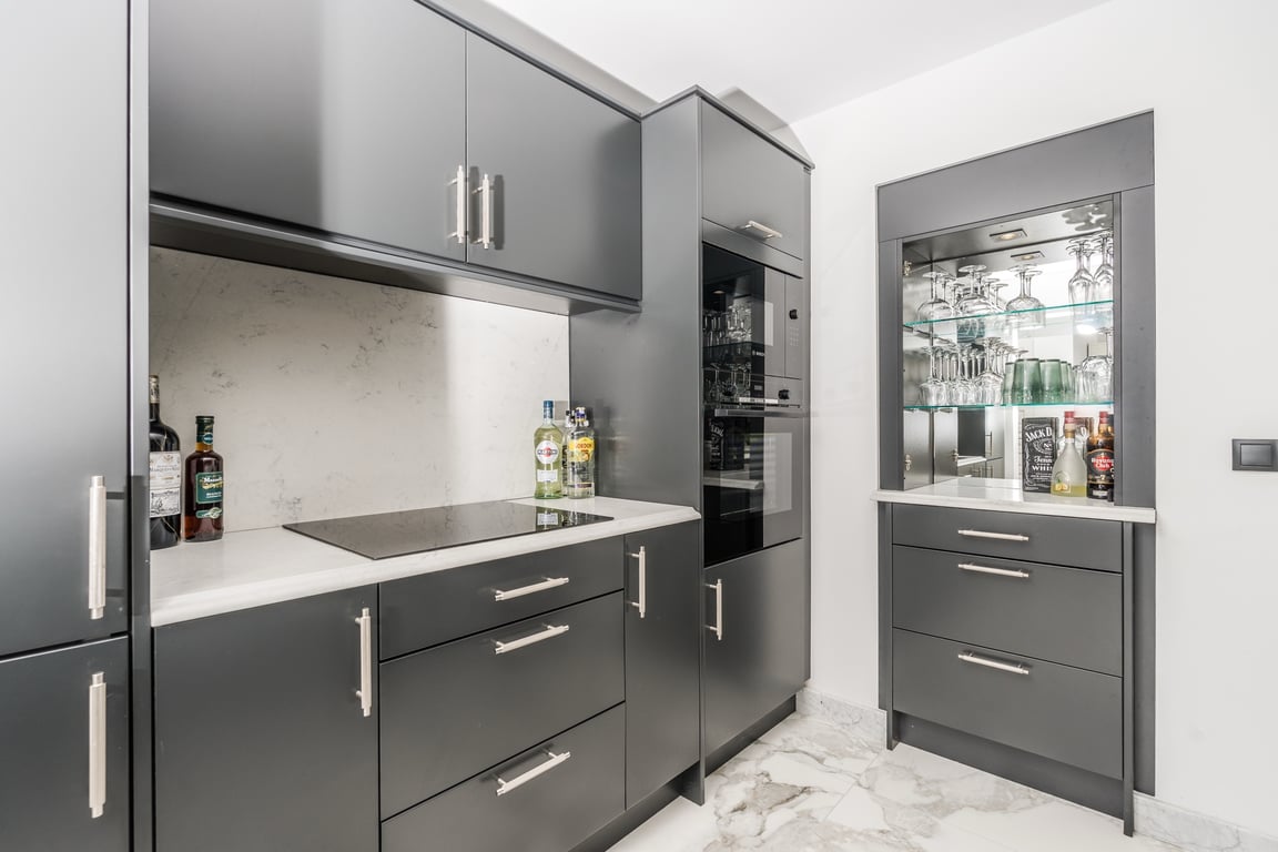 Cuisine moderne avec meubles gris anthracite, plans de travail en marbre blanc et bar intégré avec vitrine éclairée. Le sol est revêtu de marbre veiné élégant.