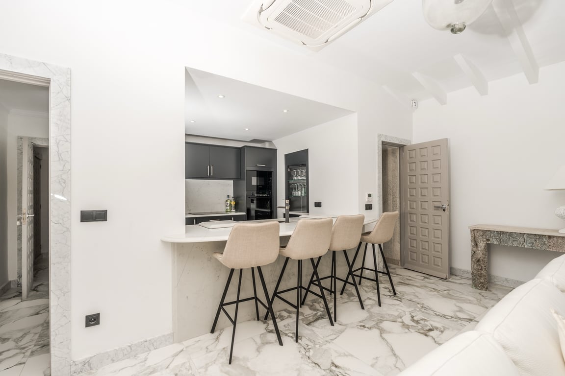 Cuisine semi-ouverte avec bar en marbre et quatre tabourets. Le sol en marbre veiné et les cadres de porte en pierre complètent cet espace moderne et lumineux.