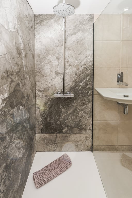 Douche à l'italienne avec parois en marbre gris, pomme de douche à effet pluie en chrome et receveur blanc épuré derrière une paroi vitrée.