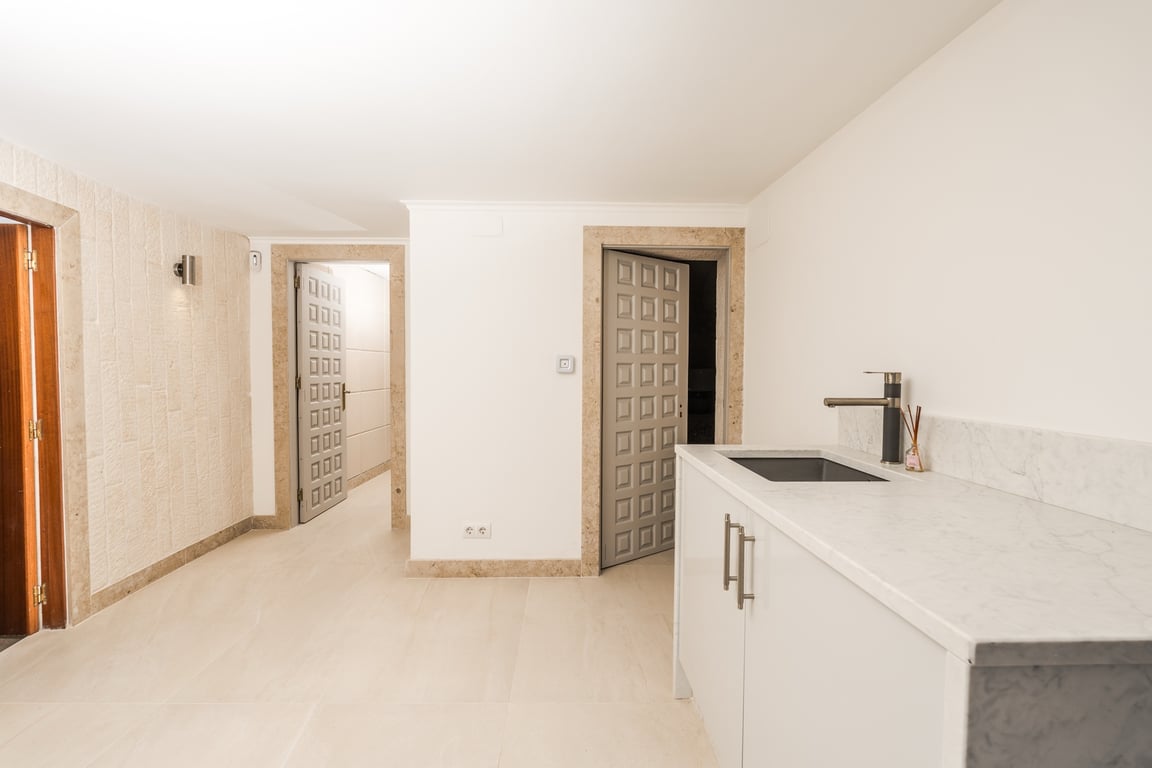 Espace de passage avec plan de travail en marbre et évier. Les encadrements de portes en pierre naturelle et les portes grises offrent un style épuré.