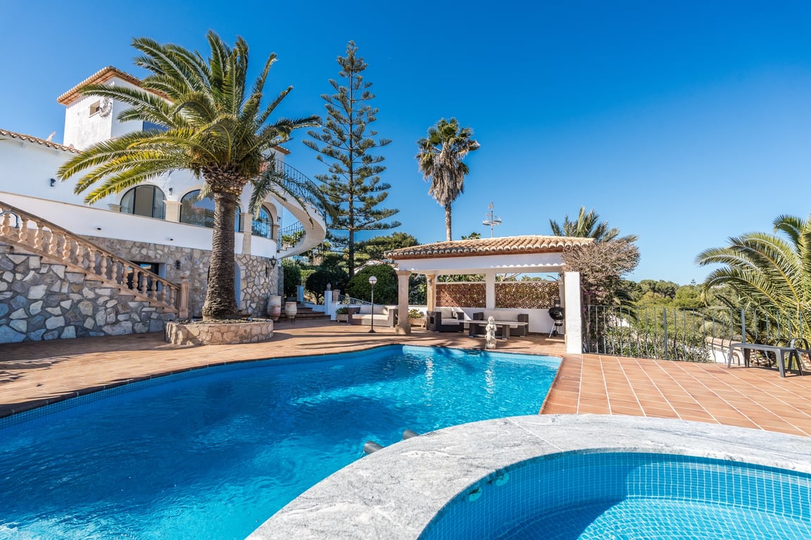 Espace extérieur avec piscine et jacuzzi, terrasse en terre cuite et jardin méditerranéen bordant une villa en pierre avec porche couvert et escalier classique.