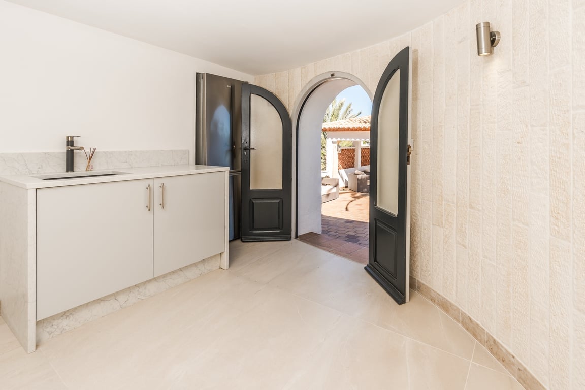 Kitchenette compacte avec plan de travail en marbre et murs en pierre naturelle, s'ouvrant sur la terrasse par une porte voûtée à double battant.