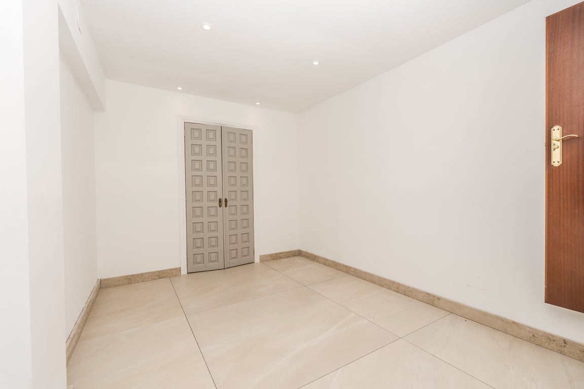 Pièce lumineuse avec sol en marbre grand format, éclairage encastré et double porte décorative grise présentant un motif géométrique élégant.