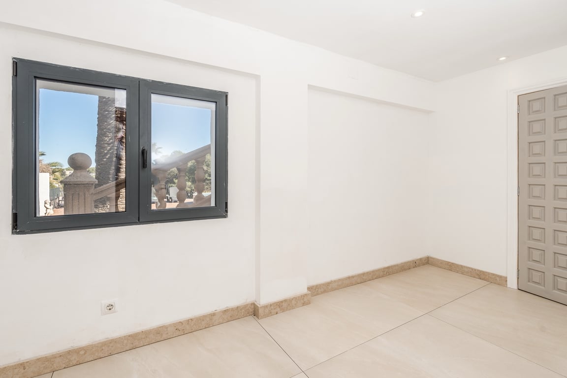 Pièce rénovée avec sol en pierre naturelle, spots encastrés et fenêtre en aluminium sombre offrant une vue sur l'extérieur de la villa.