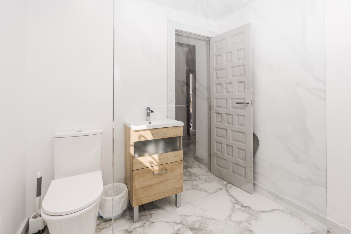 Salle de bain moderne avec carrelage effet marbre blanc, meuble sous-vasque en bois clair et paroi de douche en verre fixe.