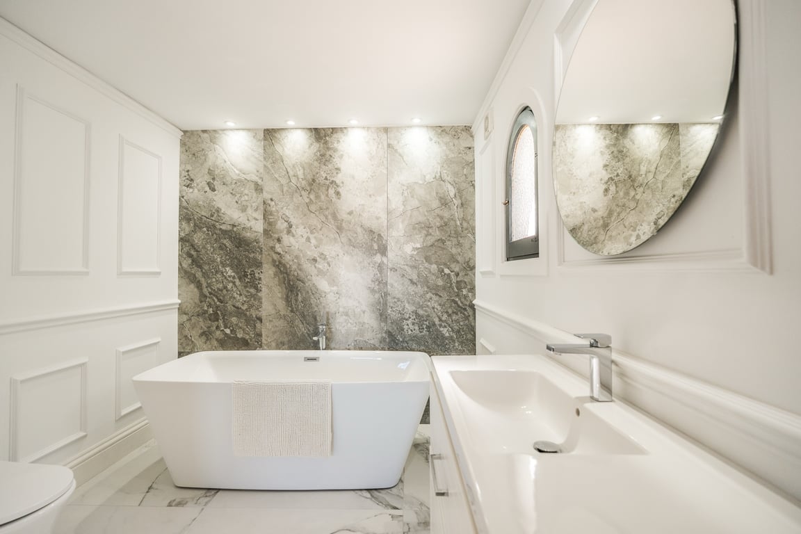 Salle de bain raffinée avec baignoire îlot, mur en marbre rétroéclairé et finitions en boiseries blanches élégantes.