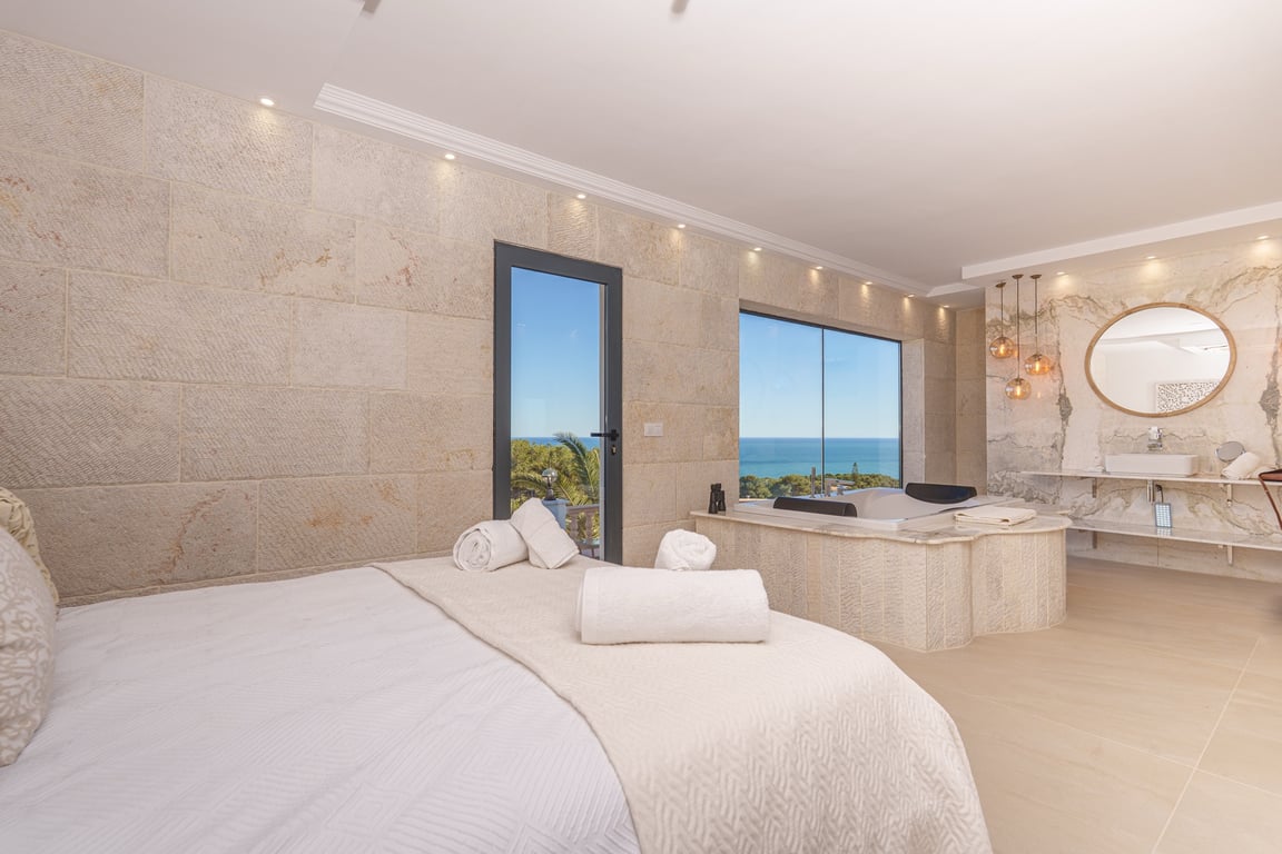 Suite parentale avec murs en pierre naturelle, jacuzzi intégré face à la mer et salle de bain à aire ouverte avec finitions en marbre.