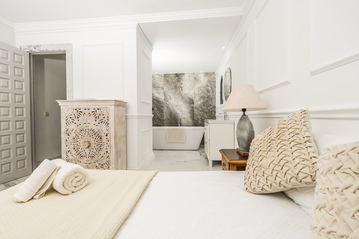 Suite parentale avec salle de bain ouverte, baignoire îlot devant un mur en marbre gris et moulures murales élégantes.