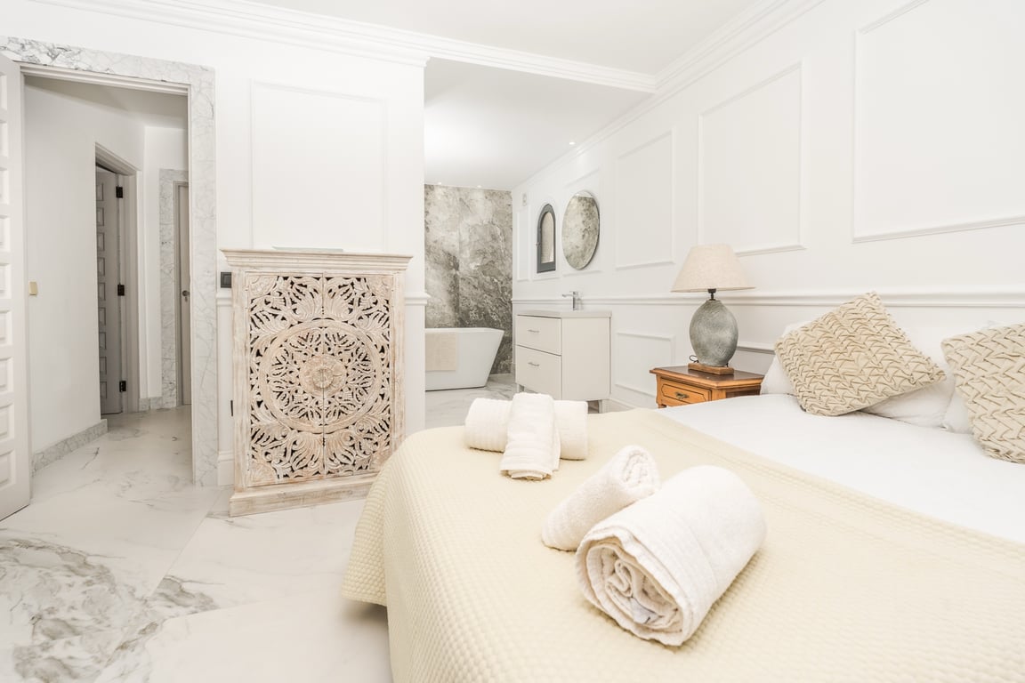 Suite parentale avec salle de bain ouverte, baignoire îlot et mur en pierre naturelle. Les sols en marbre et les moulures murales apportent une finition raffinée.