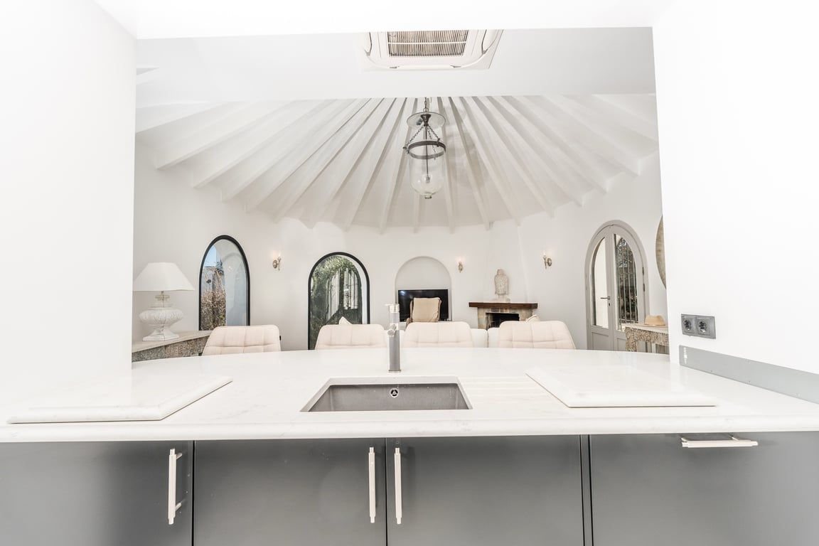 Vue depuis l'îlot de cuisine vers le salon circulaire, avec son plafond à poutres radiales blanches et ses ouvertures en arche.
