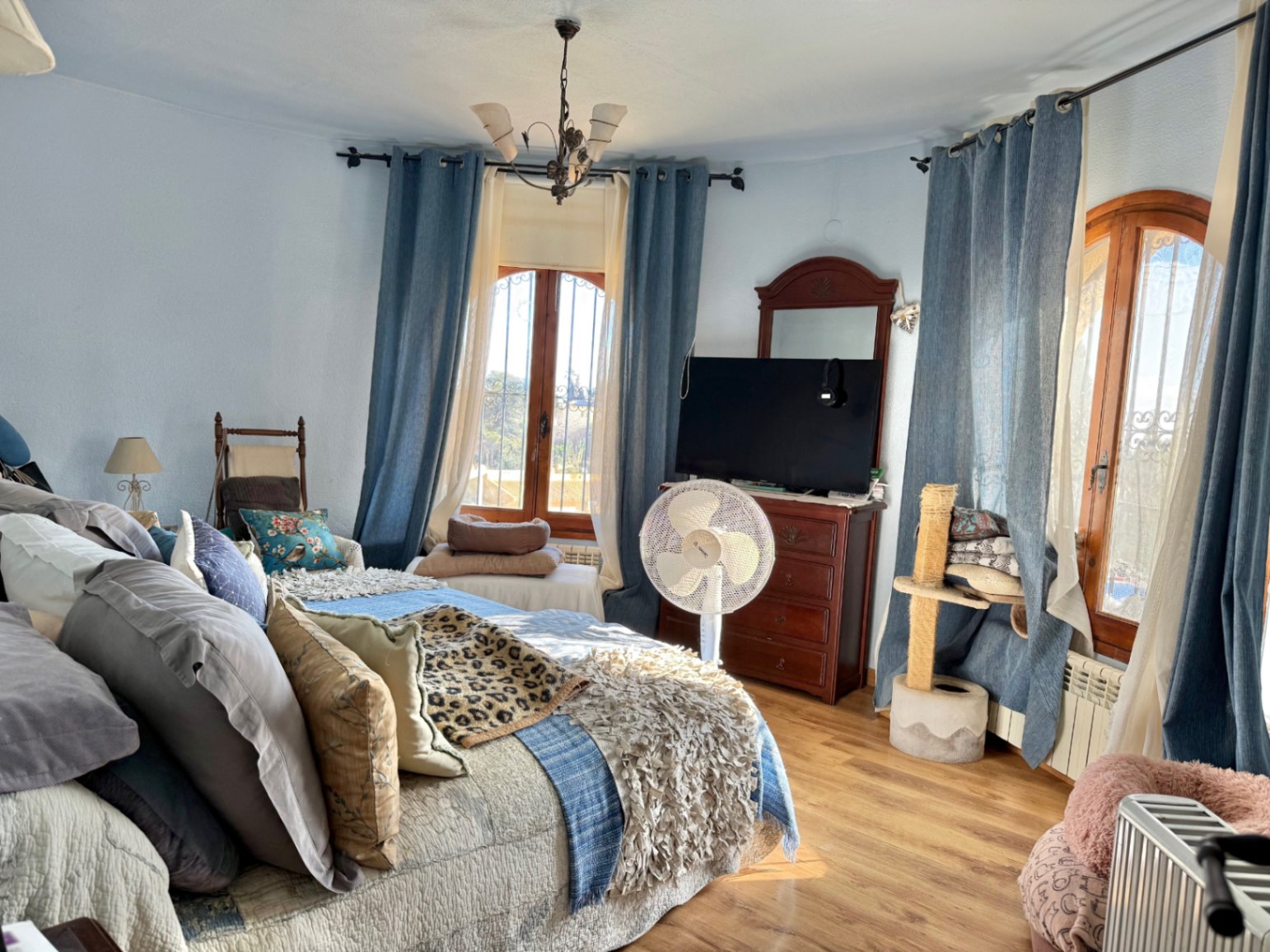 Chambre lumineuse avec mur incurvé, fenêtres cintrées en bois et sol stratifié. Elle dispose de meubles en bois classiques et d'une belle lumière naturelle.
