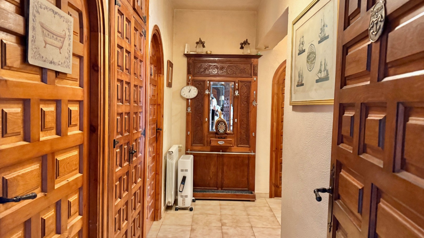 Couloir de distribution avec portes en bois massif de style castillan et encadrements en arche. Comprend un meuble d'entrée sculpté et un sol en carrelage.