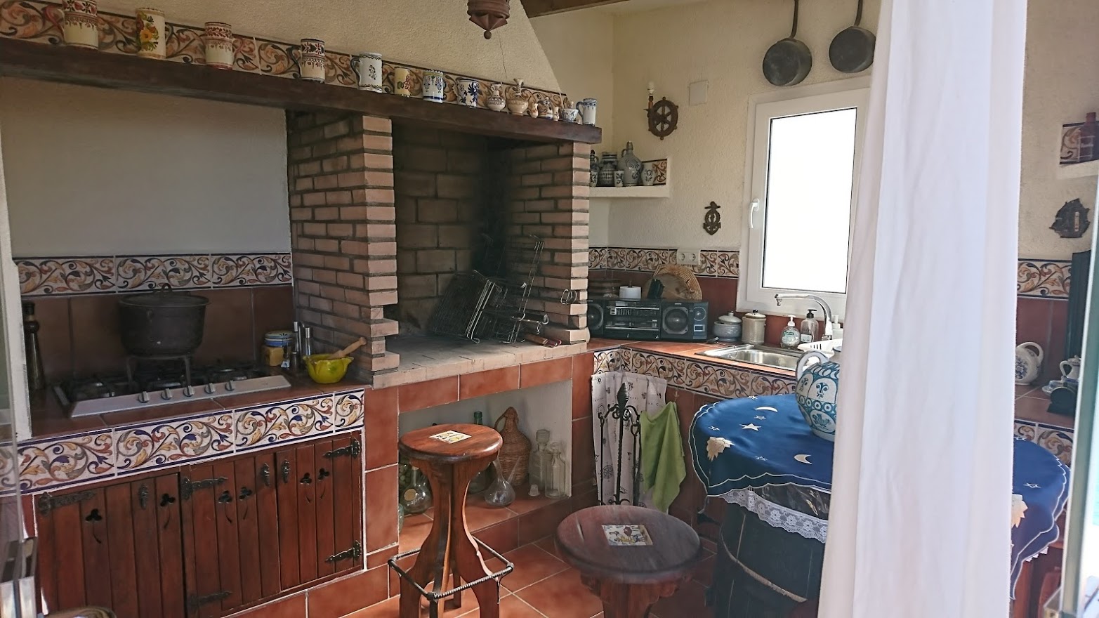 Cuisine d'été rustique avec barbecue en briques, plan de travail en carrelage traditionnel, meubles en bois et plaque de cuisson au gaz.