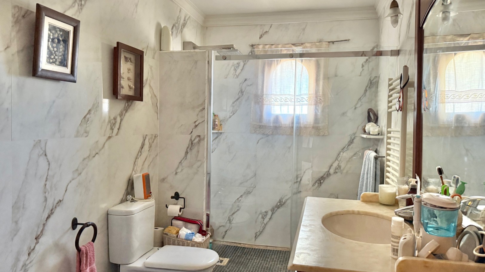 Salle de bain avec murs en carrelage effet marbre, douche à l'italienne avec paroi vitrée et fenêtre en arc. Comprend un meuble vasque et un radiateur sèche-serviettes.