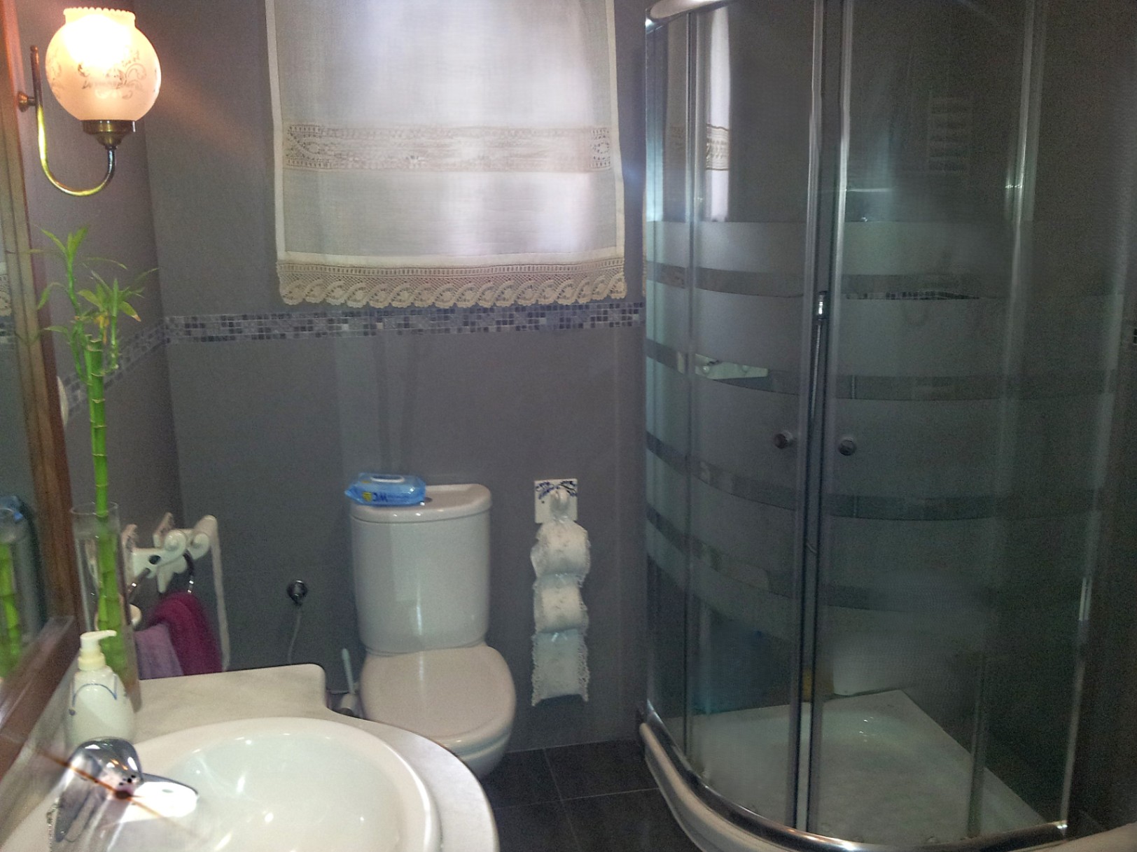 Salle de bain fonctionnelle avec cabine de douche d'angle, plan de toilette en marbre et carrelage gris agrémenté d'une frise en mosaïque.