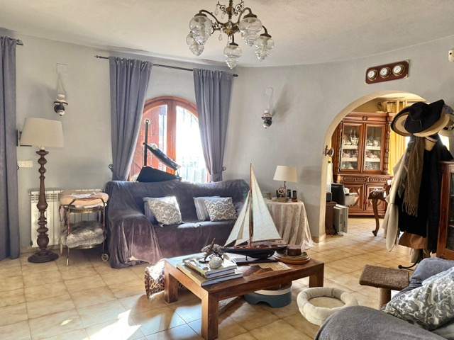 Salon aux murs incurvés avec sol en grès, fenêtre cintrée en bois et ouverture en arche vers la salle à manger, agrémenté d'une décoration thématique.