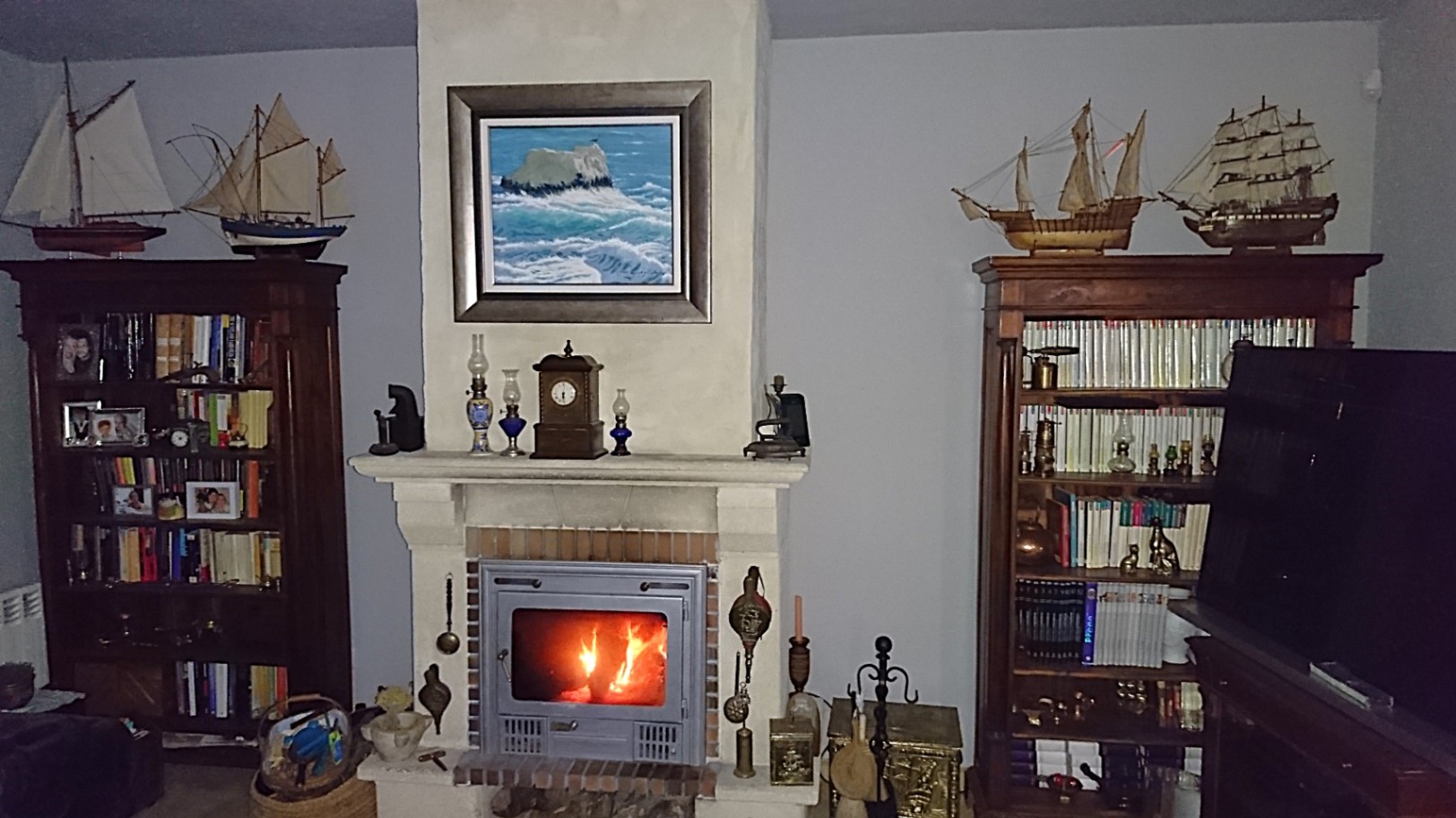 Salon traditionnel avec cheminée à insert, encadrée par des bibliothèques en bois massif ornées de maquettes de bateaux et d'objets de collection.