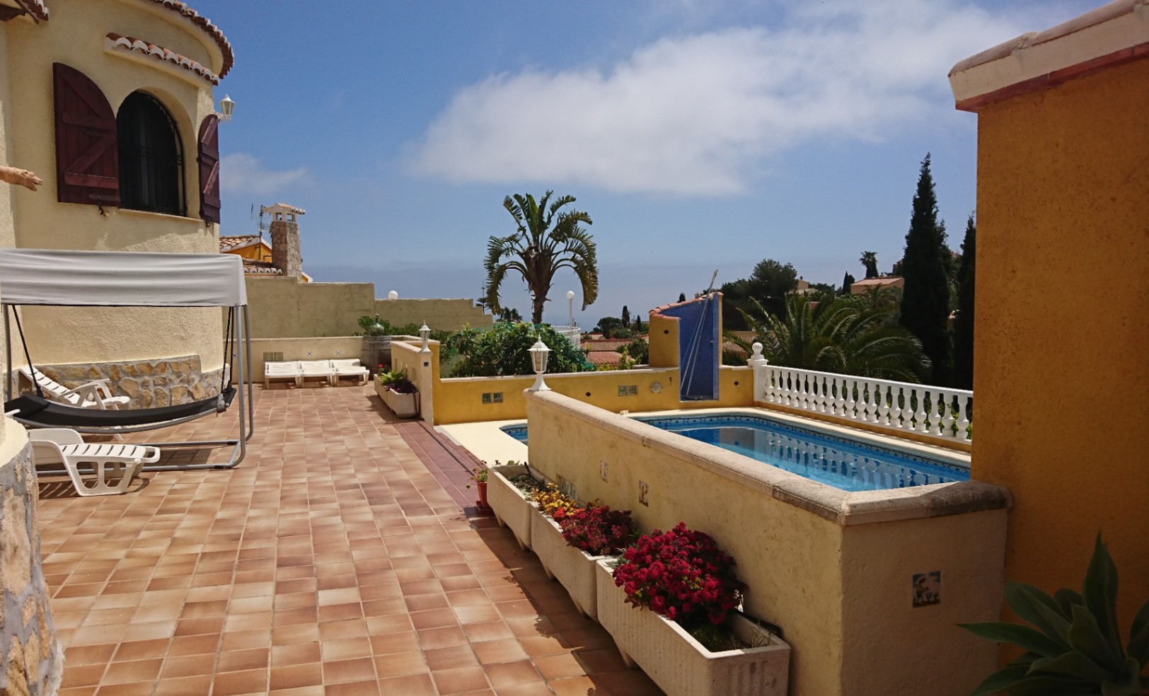 Terrasse extérieure spacieuse avec carrelage en terre cuite, piscine privée et tour de villa traditionnelle avec volets en bois et espaces de détente ensoleillés.
